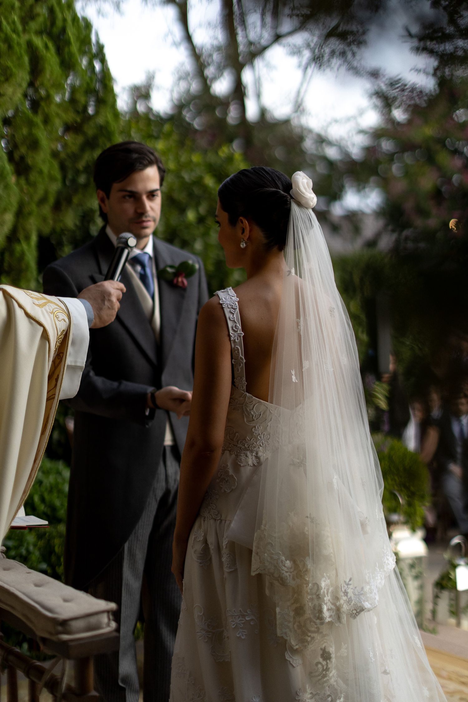 A romantic outdoor wedding ceremony shows the couple exchanging vows under trees in an elegant garden setting.