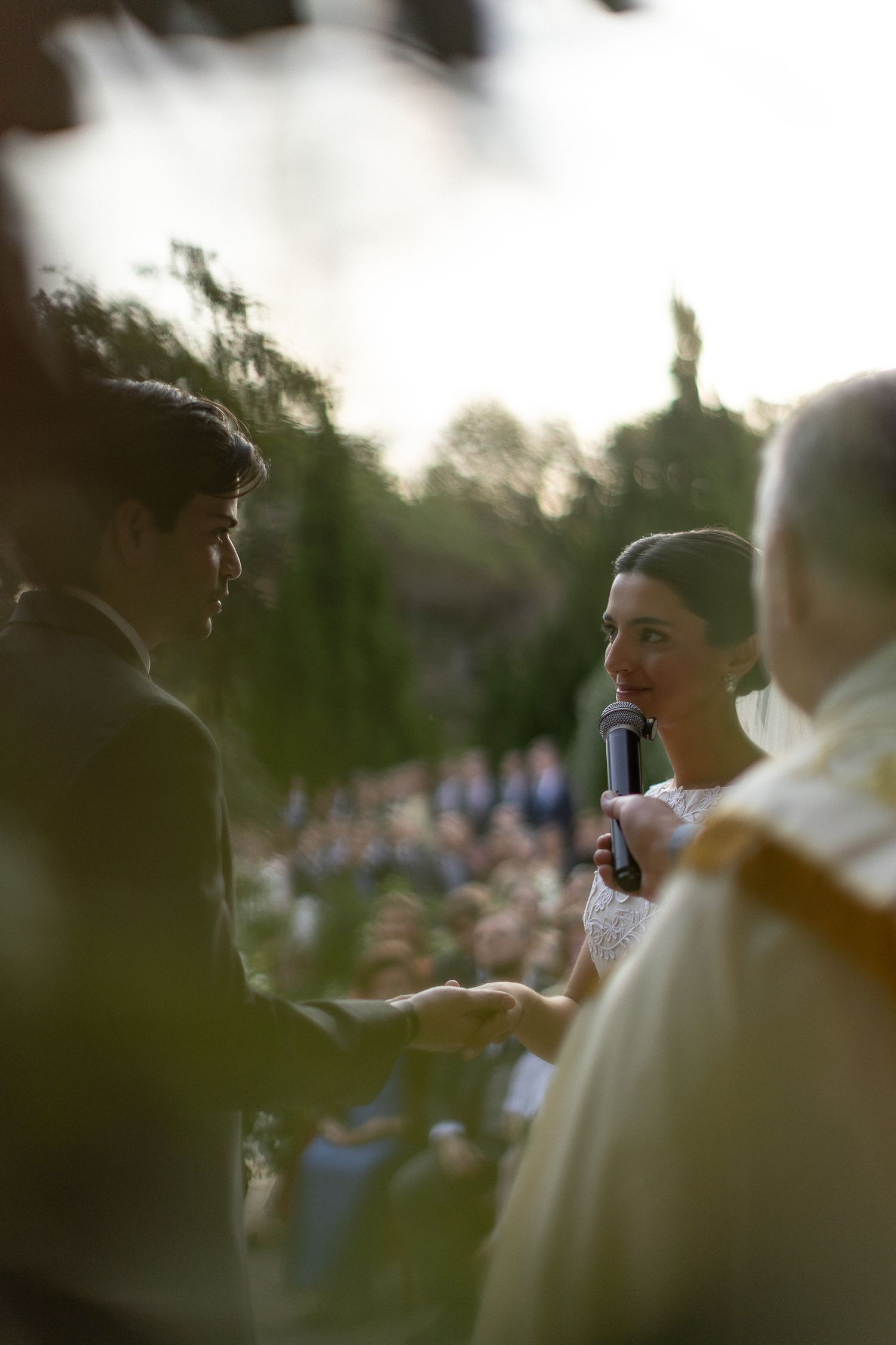 An outdoor wedding ceremony with a couple exchanging vows in front of a large crowd during golden hour.