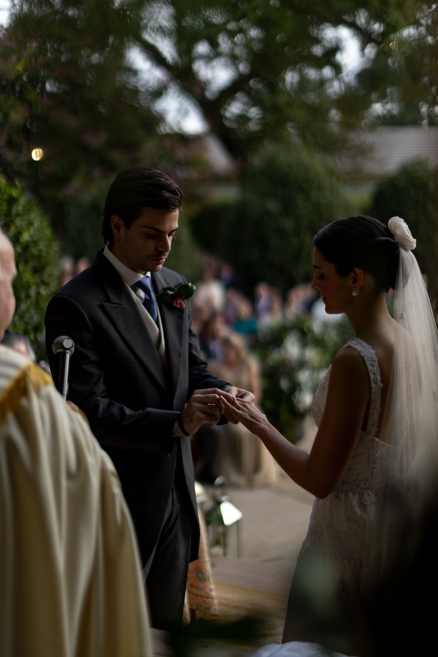 A couple exchanges rings during their wedding ceremony in a garden setting with soft natural lighting.