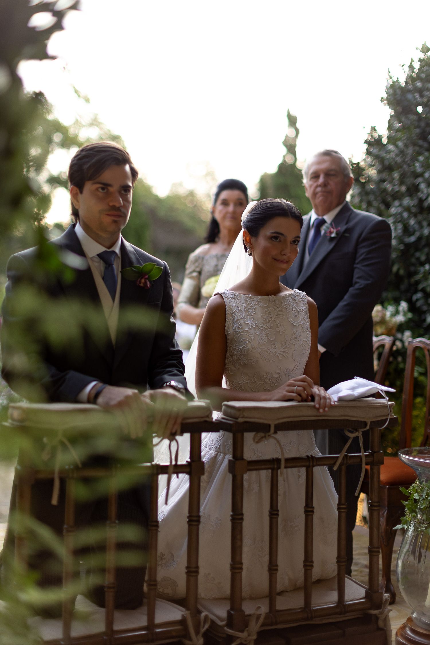 A couple sits at a rustic wooden table during an outdoor wedding ceremony signing documents.
