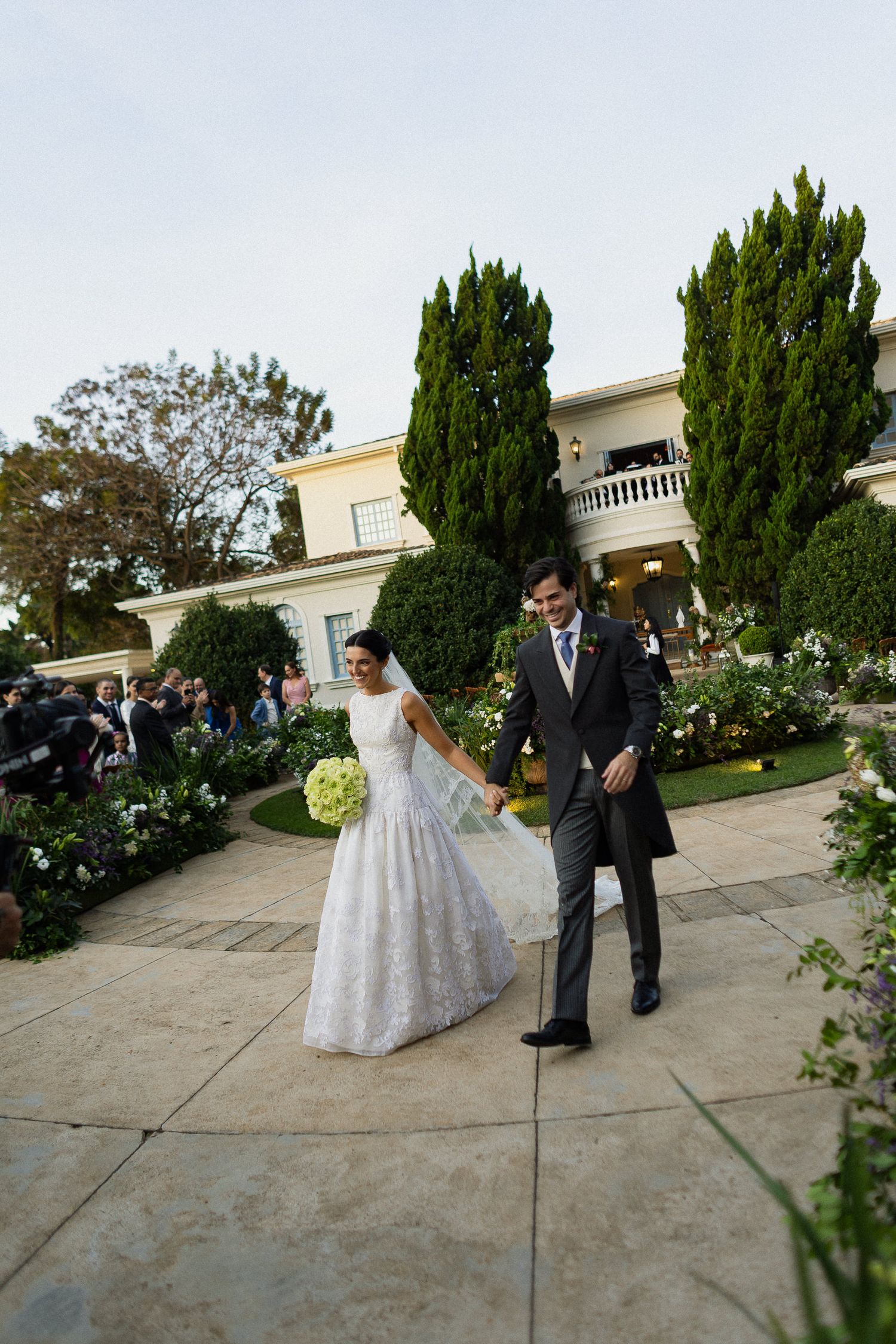 A wedding couple shares a tender moment on a garden terrace with elegant white columns and greenery in the background.