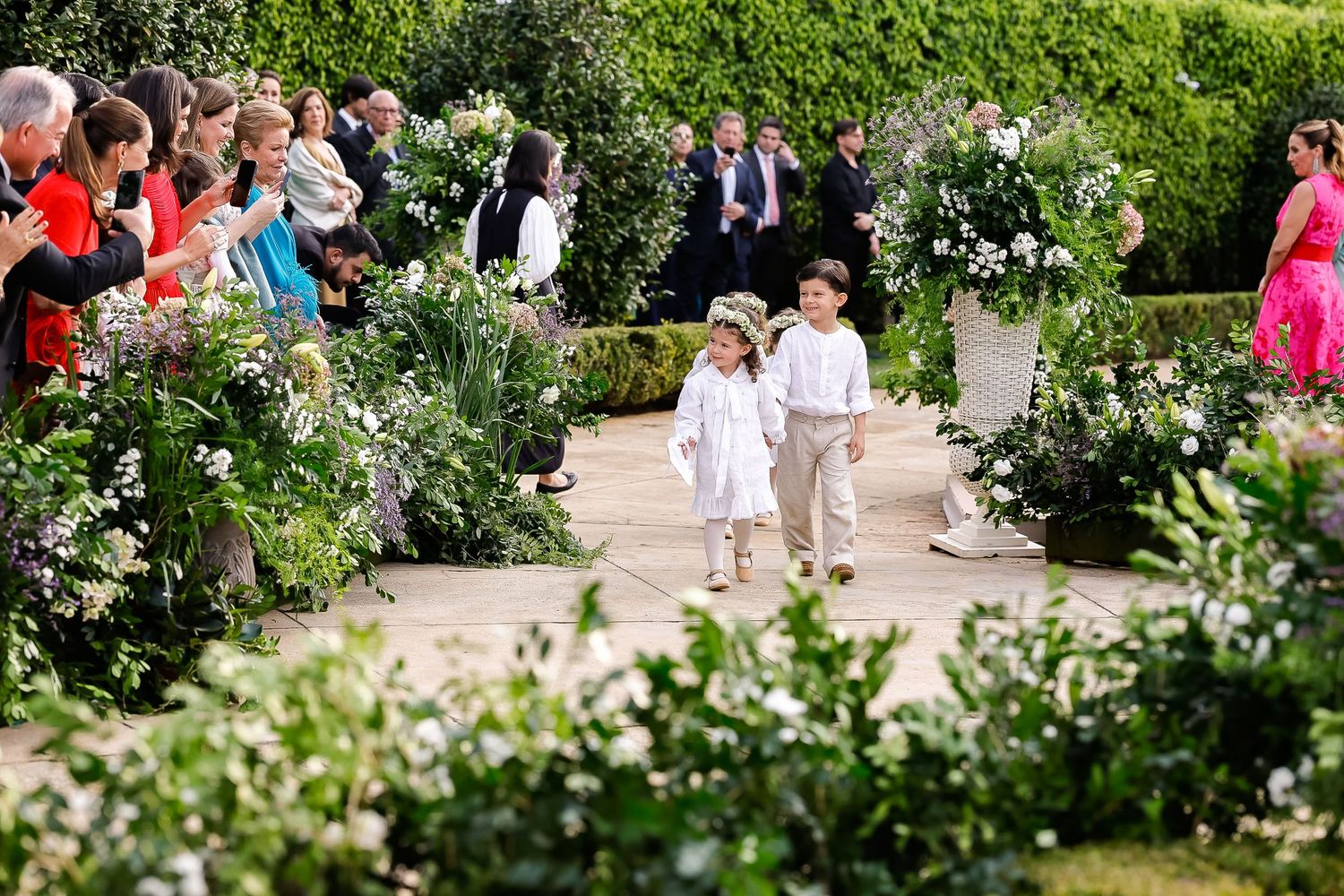 Guests gather along a garden pathway during an outdoor celebration surrounded by lush greenery and flowers.
