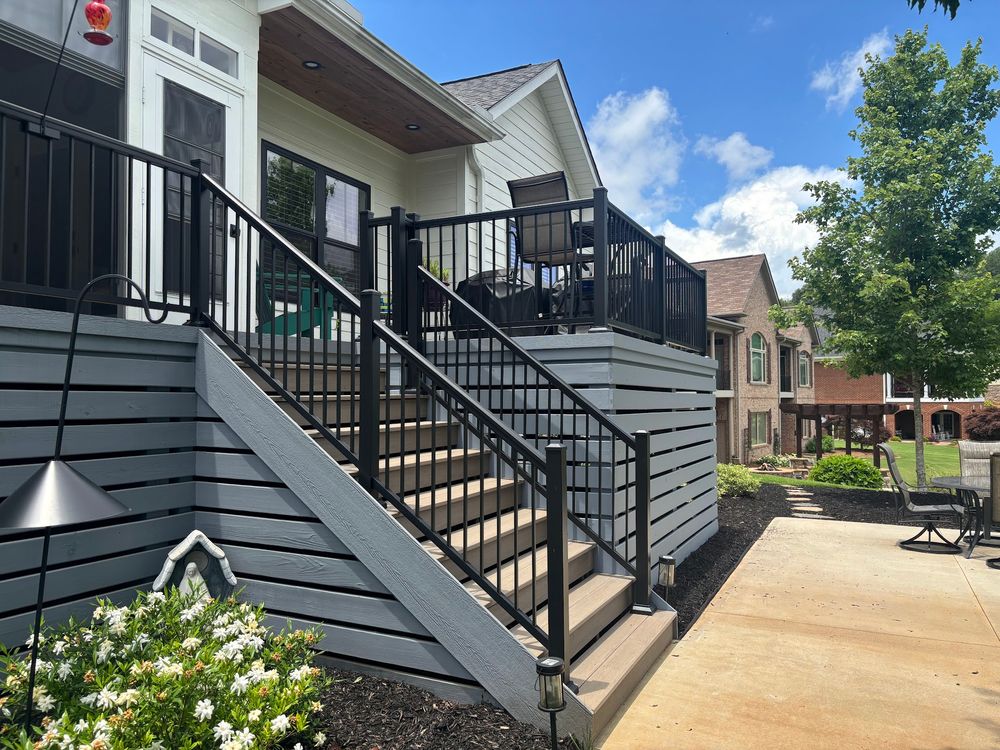 Modern deck railing installation with black aluminum balusters and white posts against blue sky and trees.