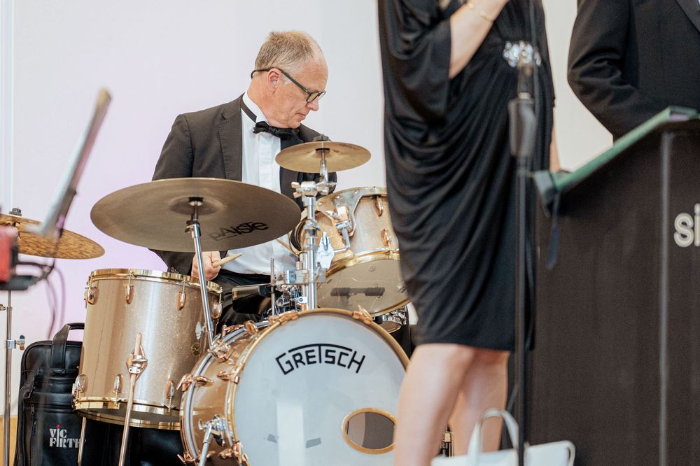A drummer performs on stage with a Gretsch drum kit during a live musical performance.