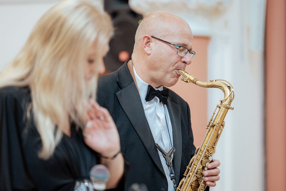 Musicians in formal attire perform on stage with saxophone and microphone during an elegant event.