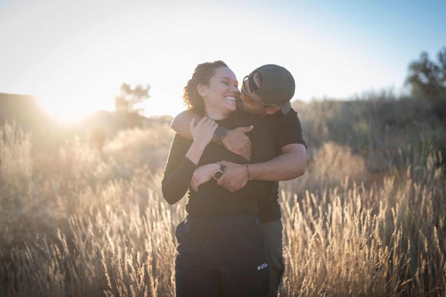 A couple embraces in a golden wheat field at sunset creating a romantic silhouette against the glowing sky.