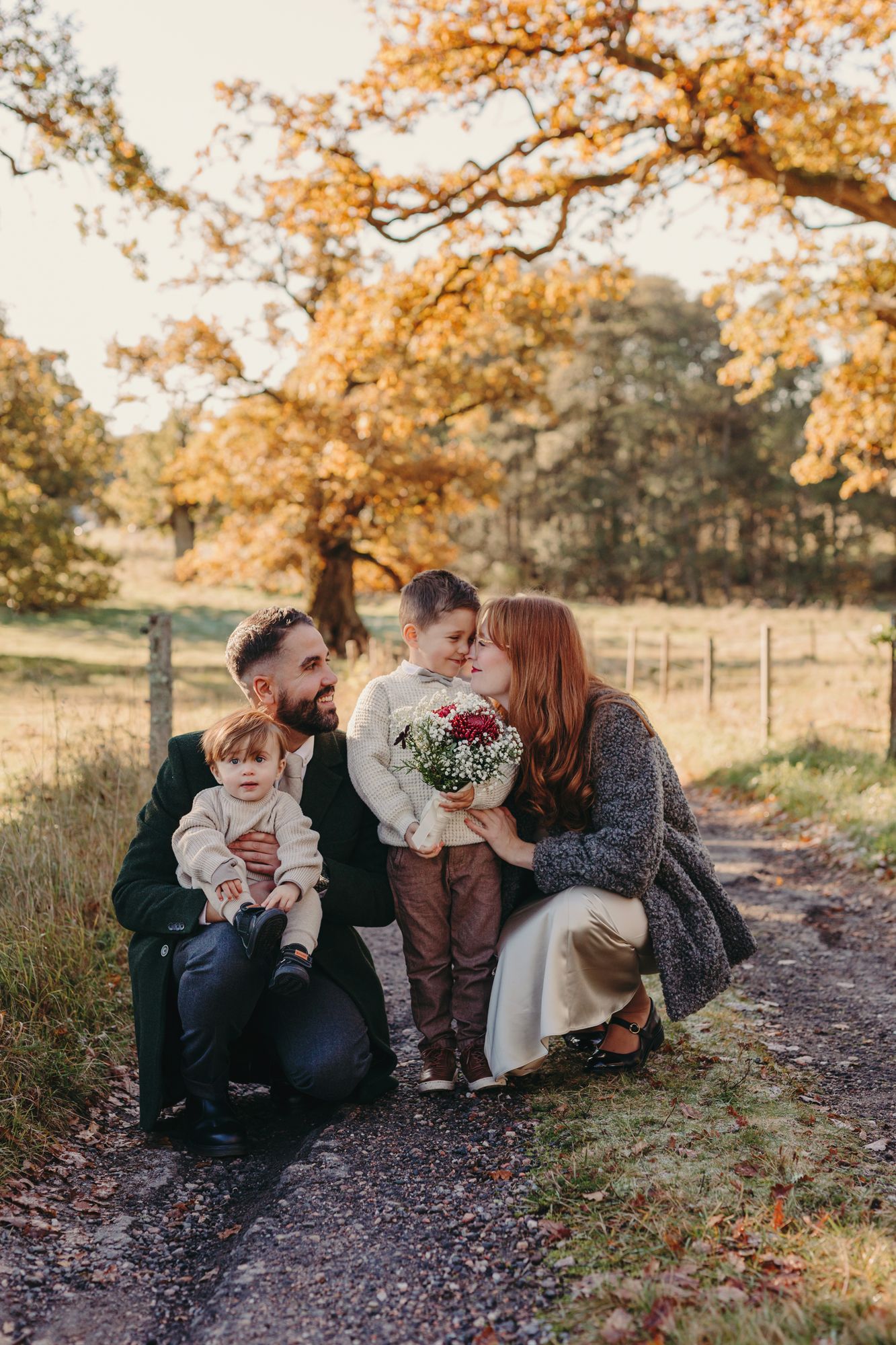 A group sits together on a path surrounded by autumn trees with golden leaves during a fall photo session.