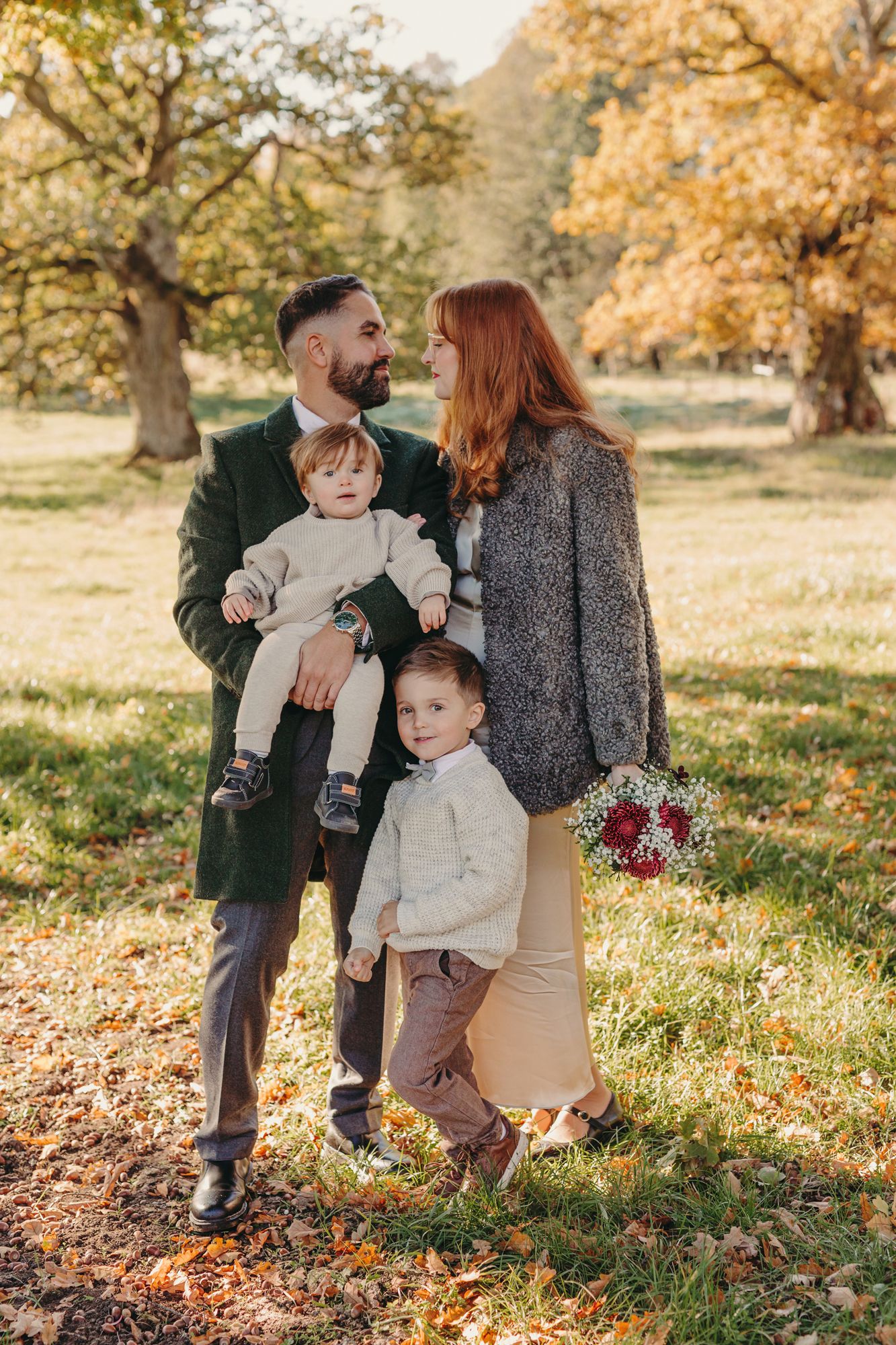 Family enjoying a warm autumn day together in a park with fallen leaves and golden sunlight filtering through trees.