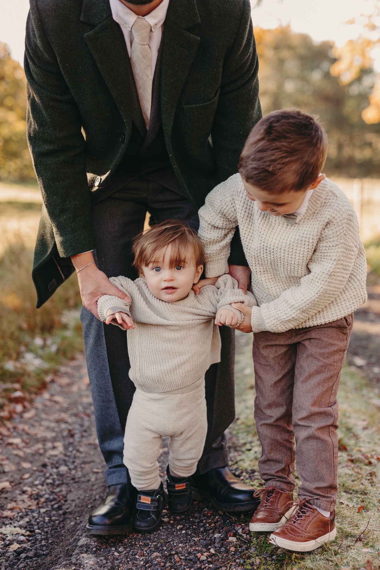A series of photos showing a parent helping a small child in a cream sweater learn to walk outdoors in autumn.