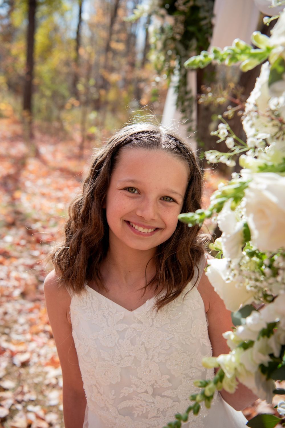 A white lace dress is photographed against a backdrop of autumn foliage and white floral decorations.