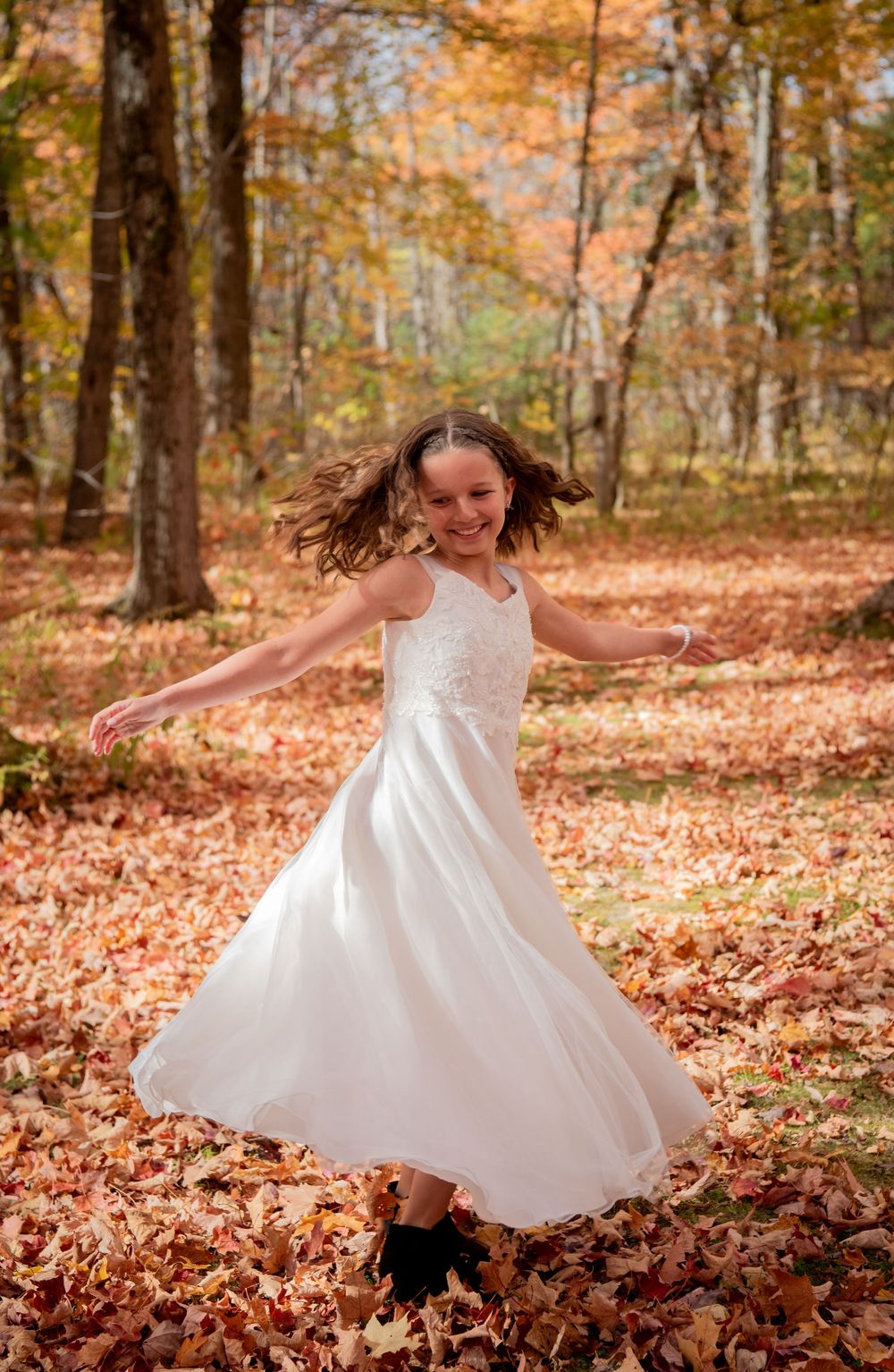 A white dress twirls through autumn leaves in a forest during a playful photo sequence.