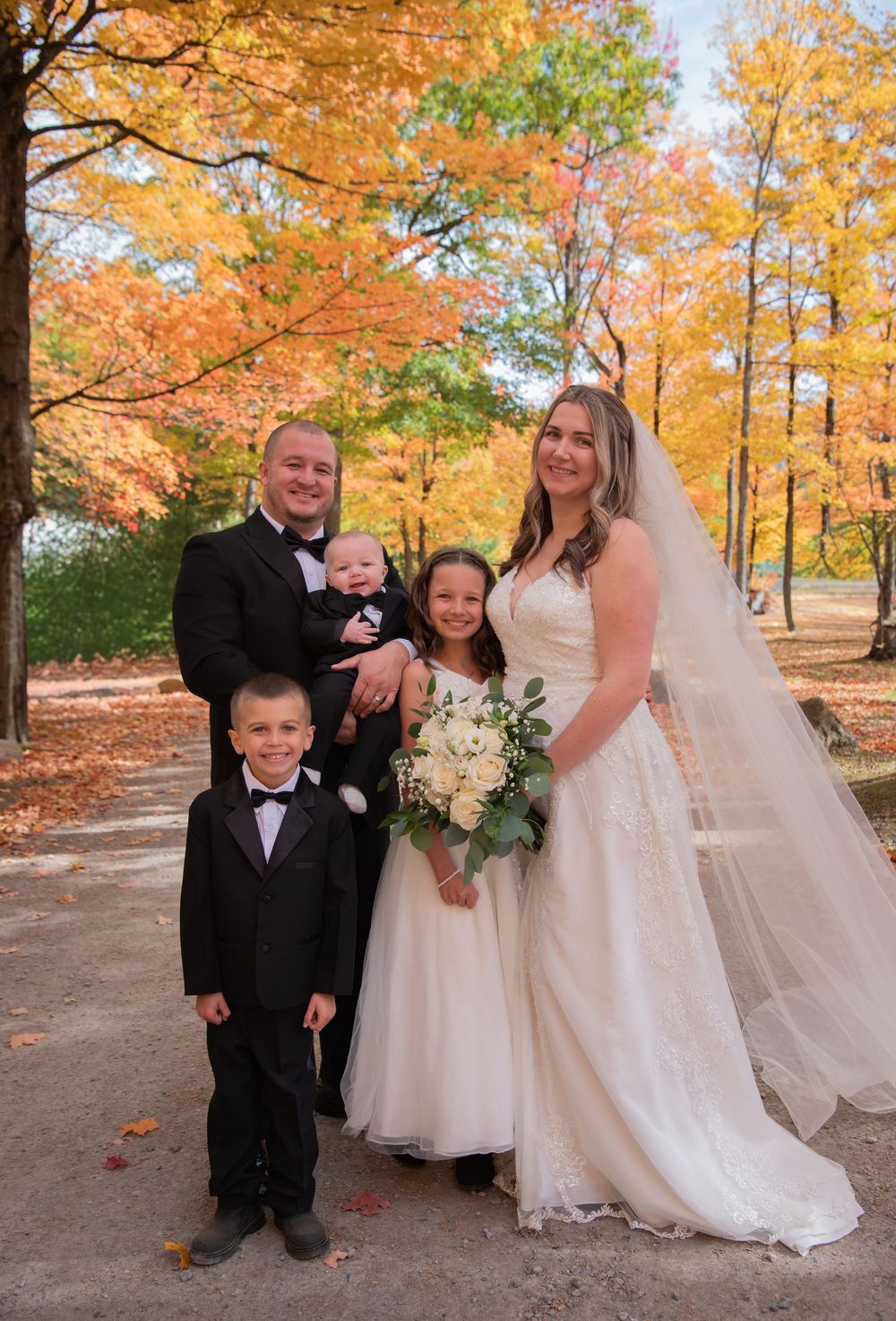 Wedding party poses together on a path surrounded by vibrant fall foliage.