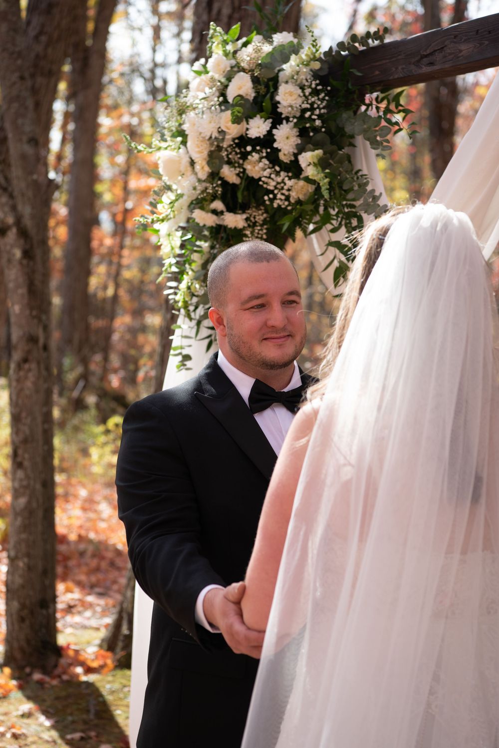 A bride and groom share an intimate moment in a wooded autumn setting during their wedding photoshoot.