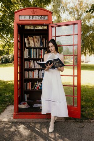 mariée qui lit devant une cabine à livres dans le parc du chateau de plaisir