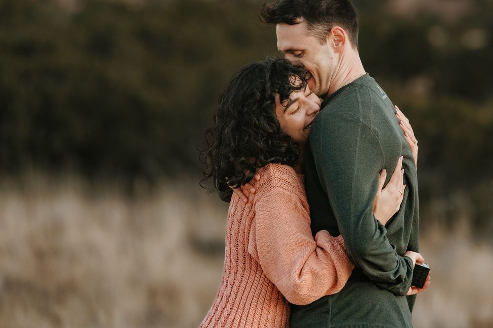 Newly engaged couple sharing a warm embrace in outdoor field after marriage proposal.