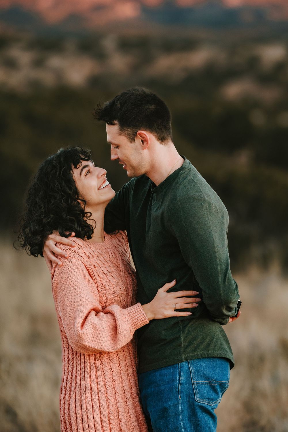 Smiling couple hugging outdoors with red rock landscape in background.