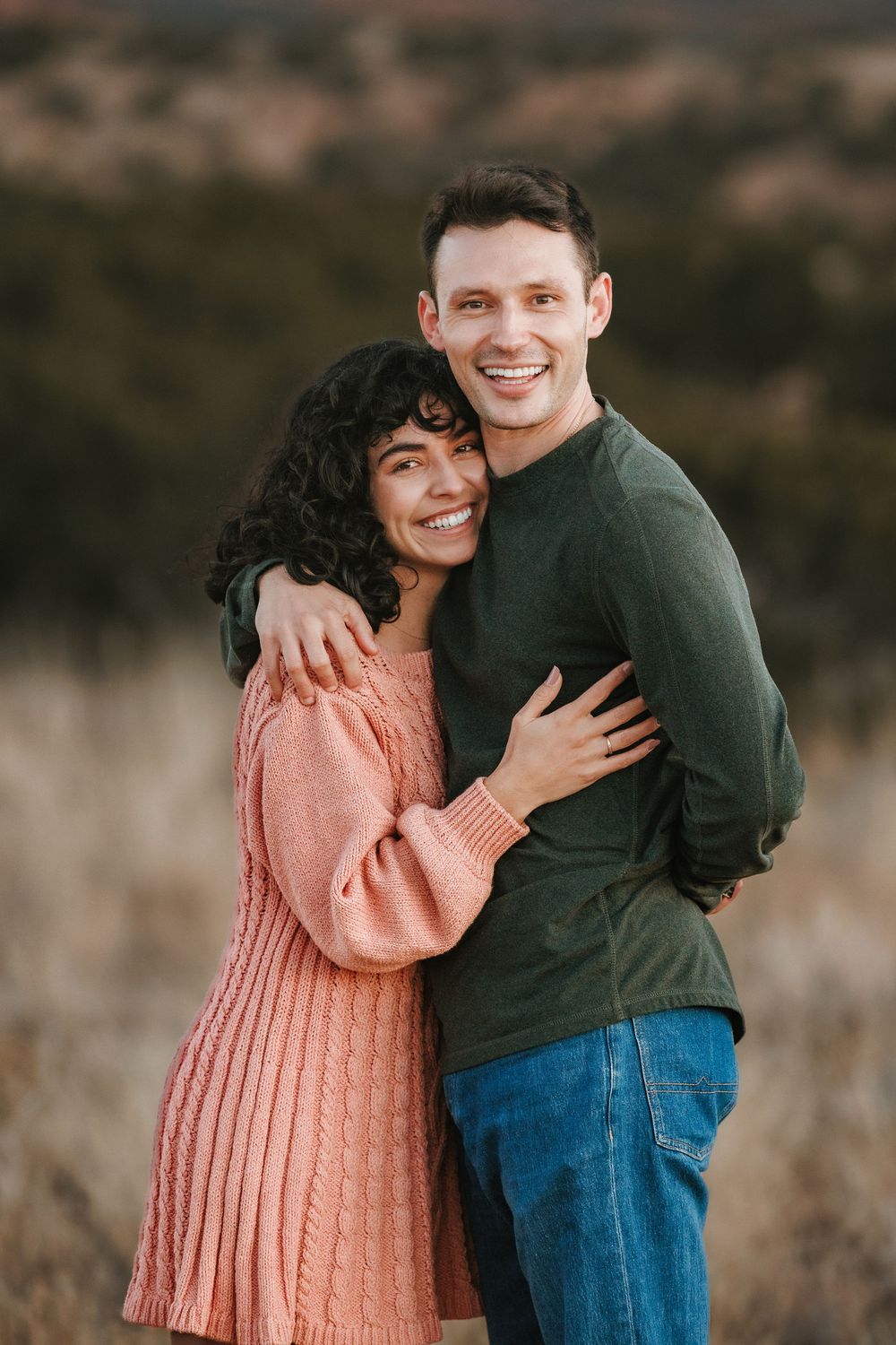Happy couple posing together in a golden field, woman in pink sweater dress.