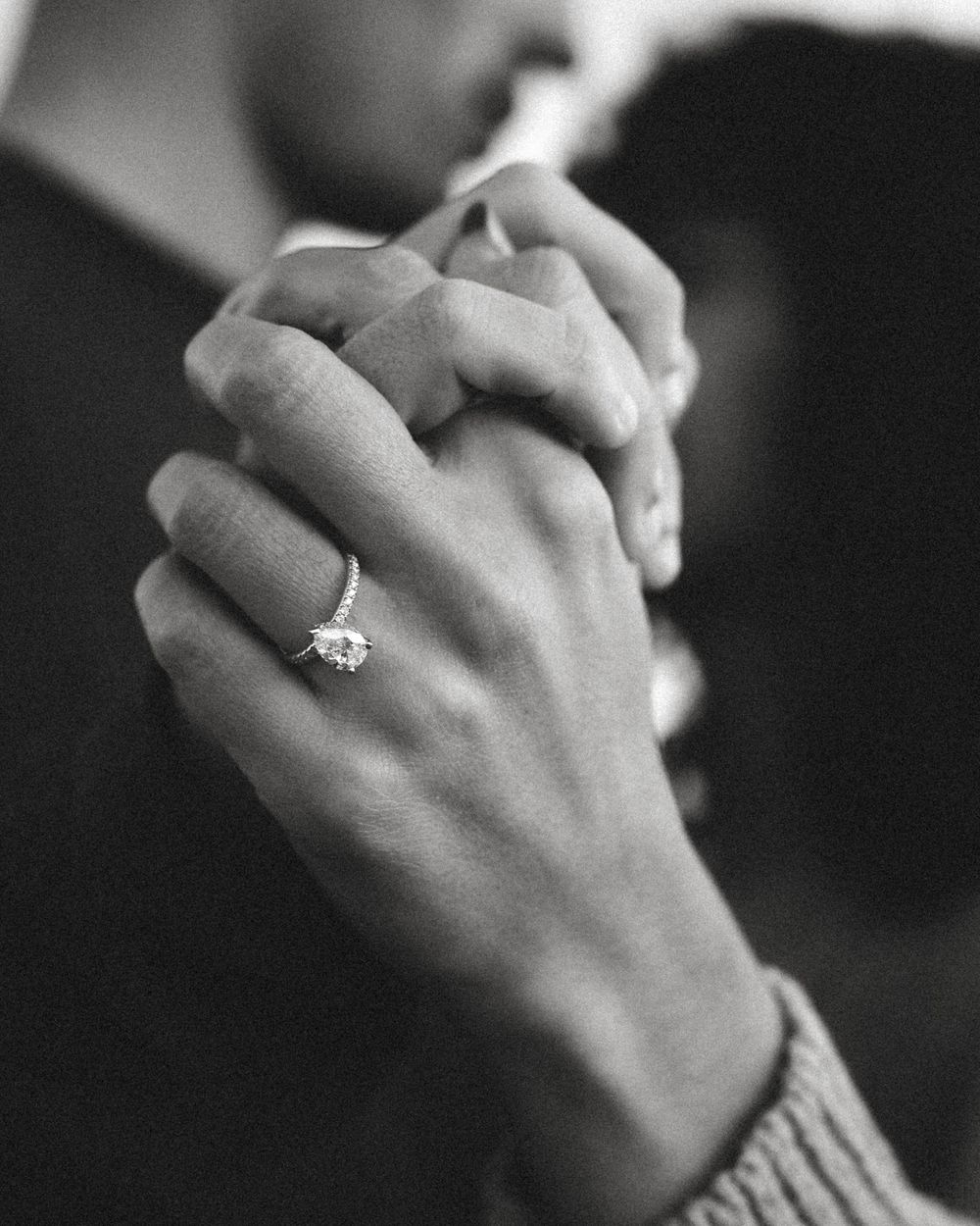 Close-up black and white photo of couple holding hands with a diamond engagement ring.