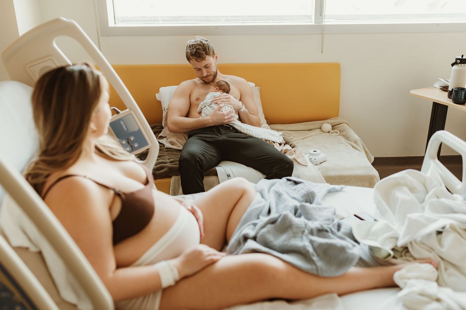 Two parents in hospital room bonding with their newborn baby while resting in bed together.