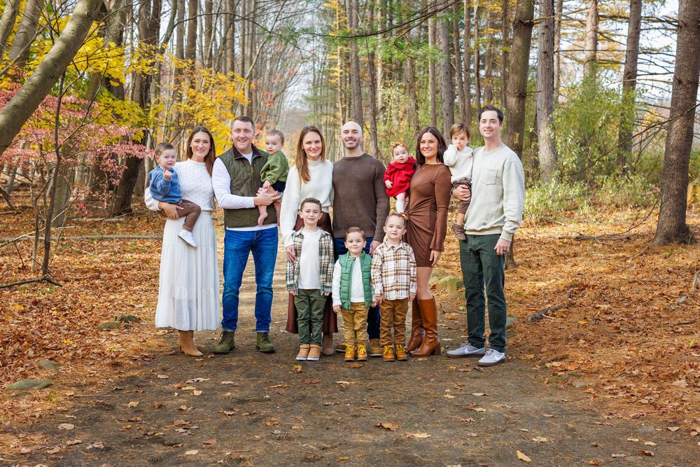 Large group gathering in wooded area with fall foliage.