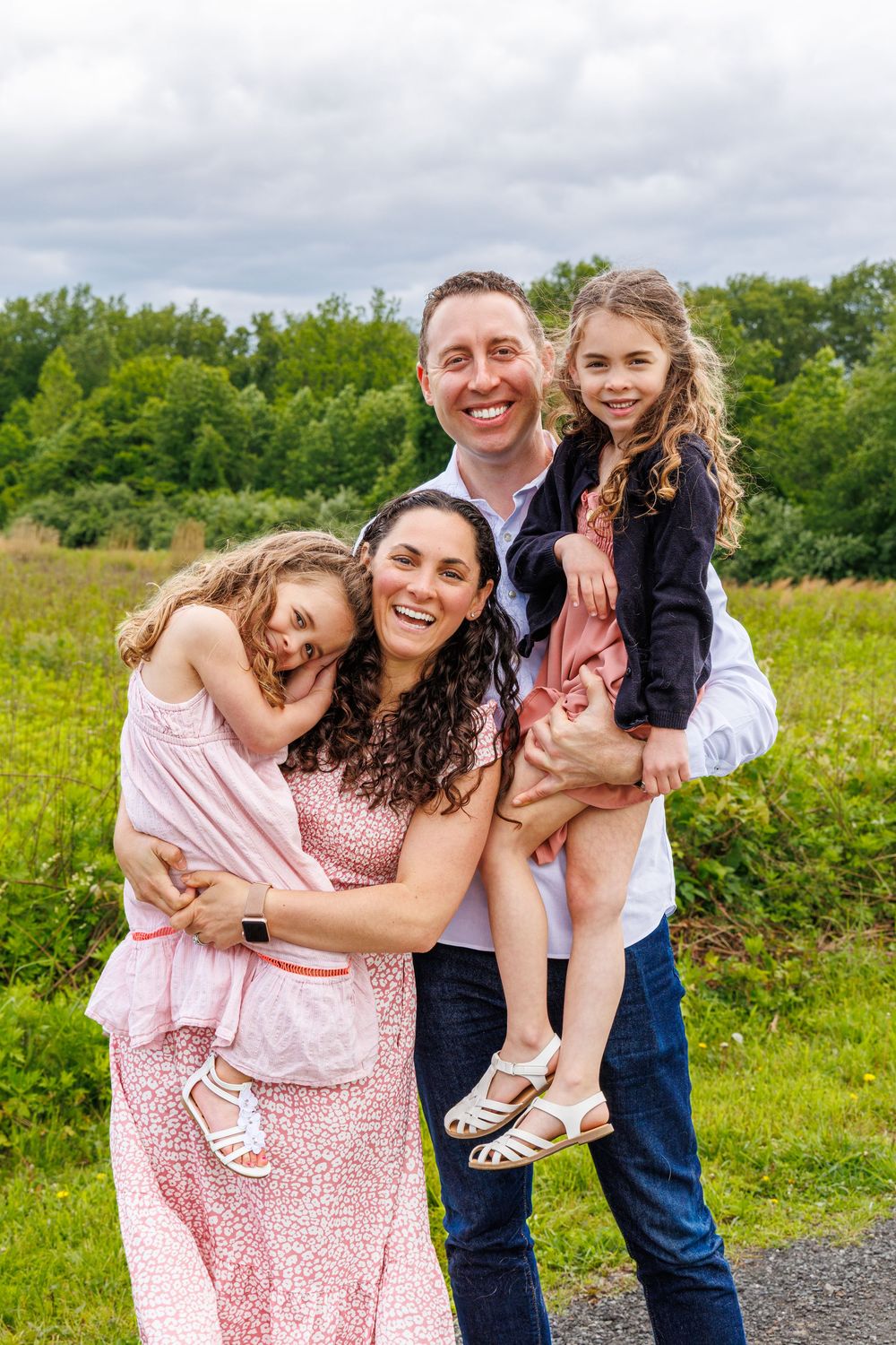 A family shares joyful moments together in a green field on a cloudy summer day, wearing pink and blue casual attire.