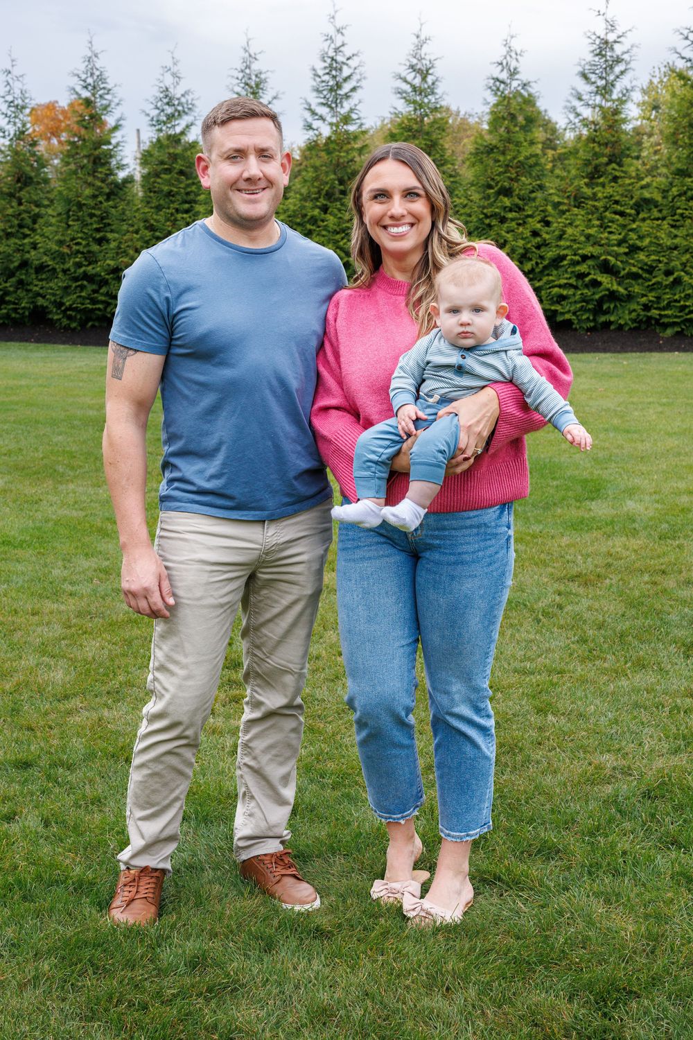 Family walking together on green grass with evergreen trees in the background.