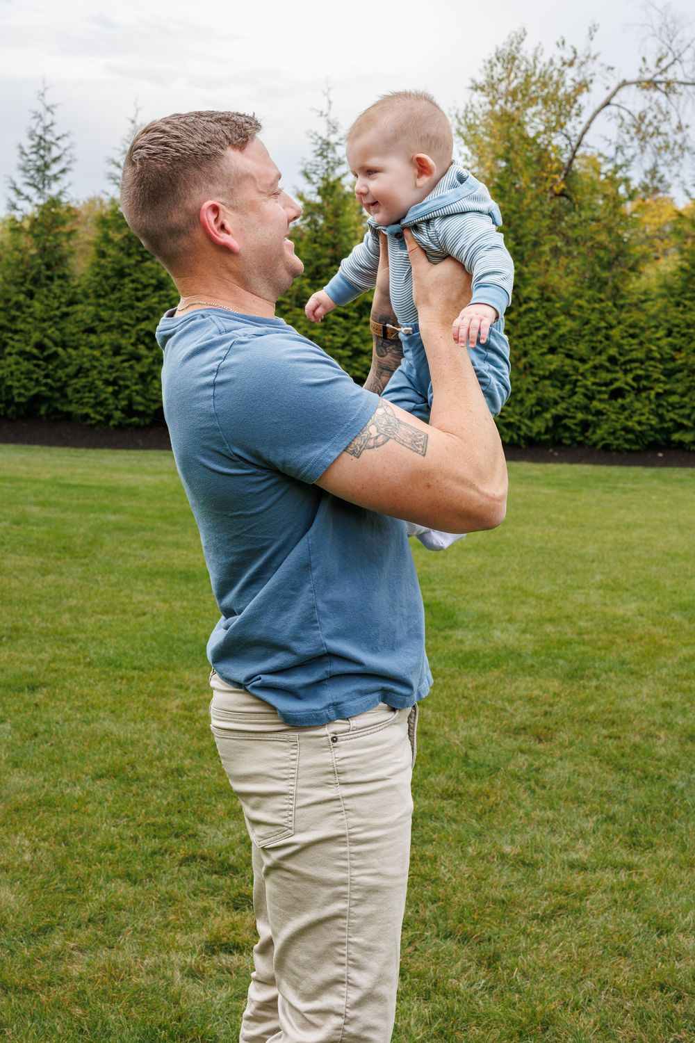 Parent playing with small child in blue clothes on a grassy lawn.