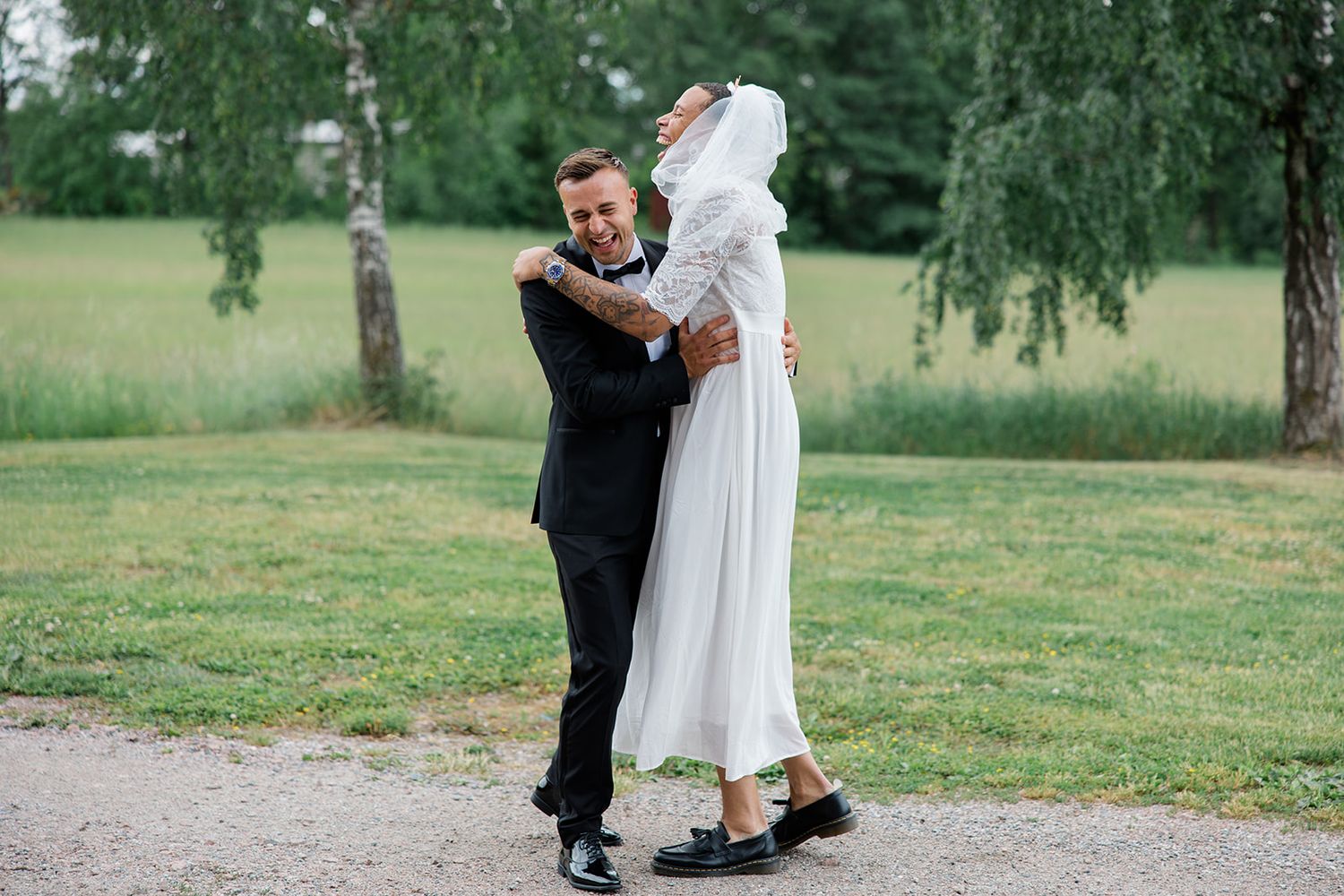 A couple in formal wedding attire dancing together on a grassy lawn during an outdoor celebration.