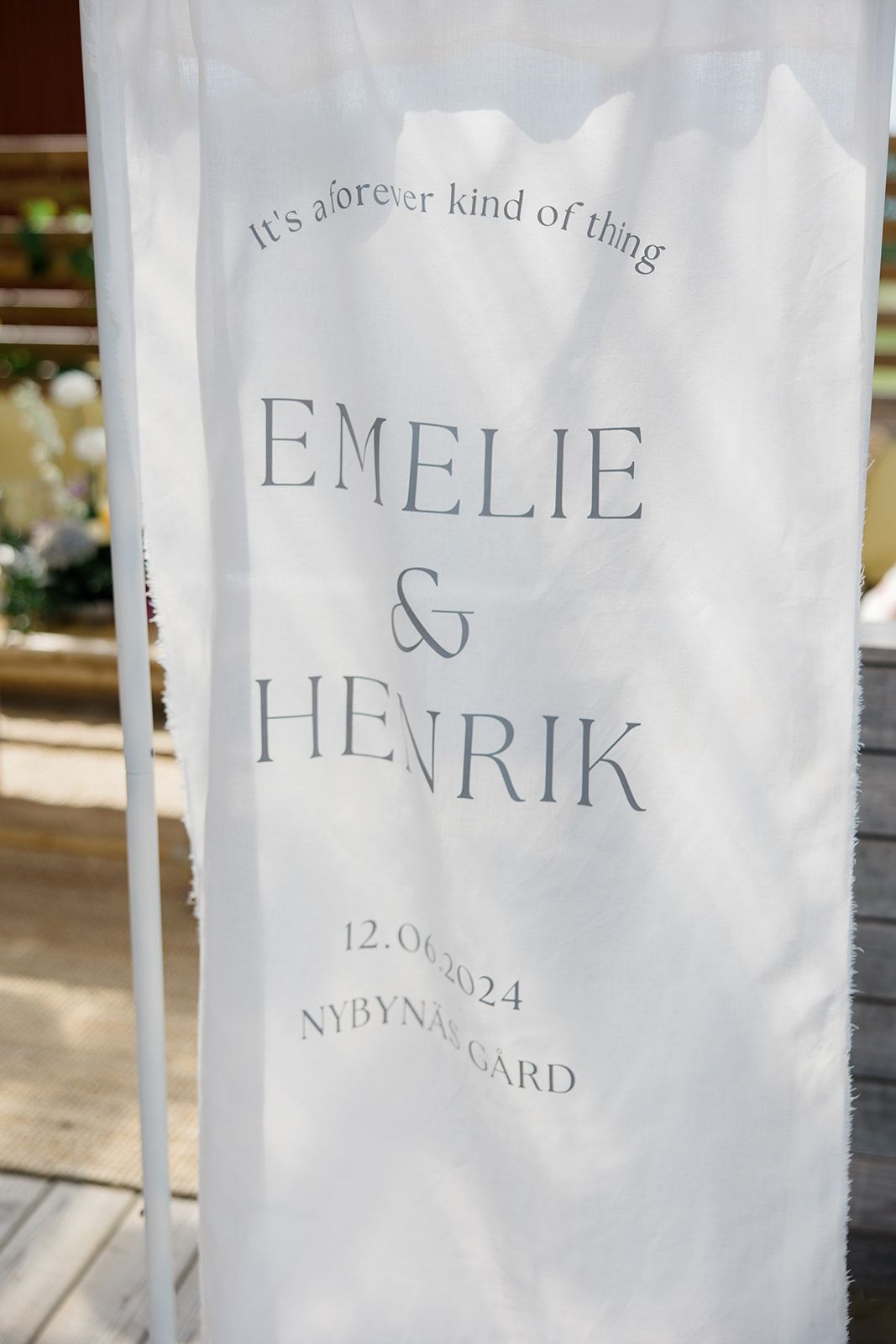 Wedding invitation details printed in elegant gray text on white fabric material showing names and date.