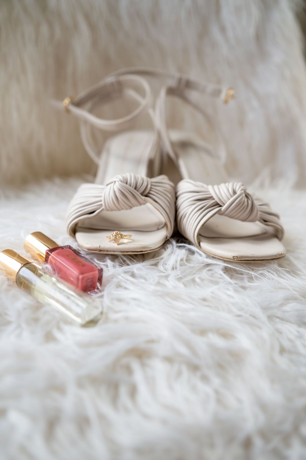 A close up detail shot of a bride's elegant nude colored heels arranged with cosmetics and accessories on white fabric background.