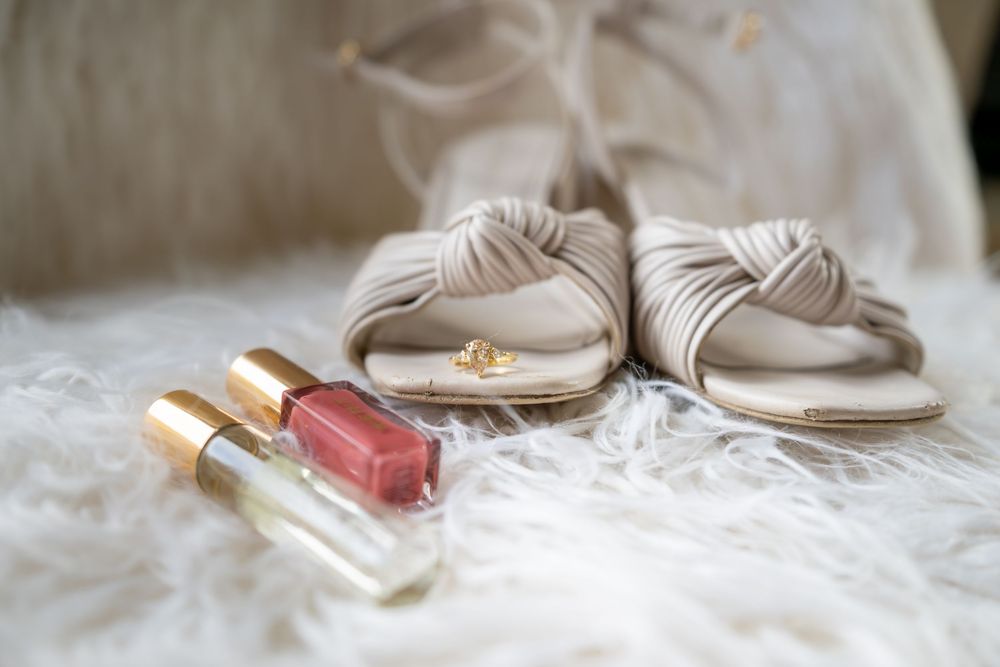 A close up detail shot of a bride's elegant nude colored heels arranged with cosmetics and accessories on white fabric background.