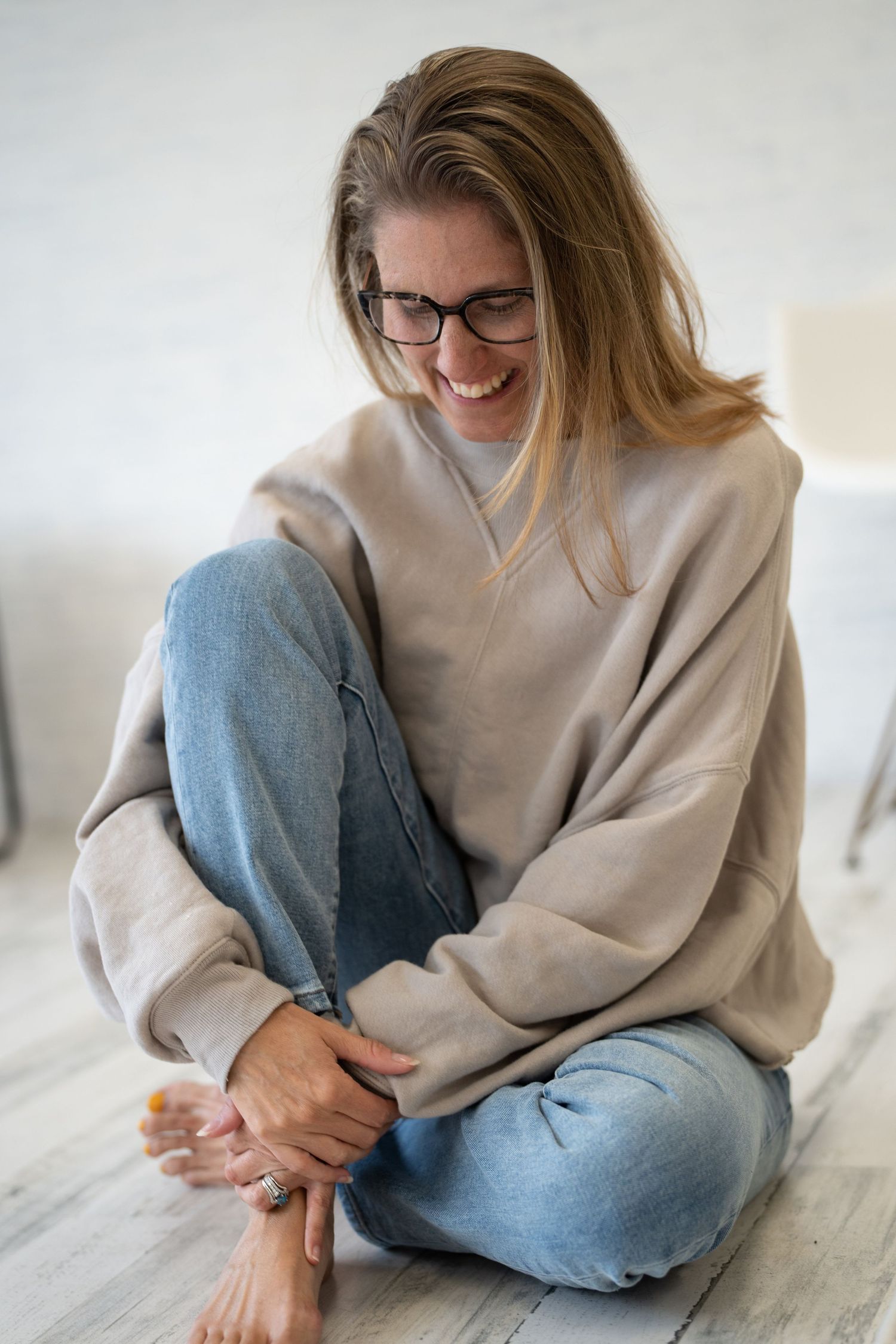 Candid lifestyle photo of person in cozy sweater and jeans relaxing on wooden floor.