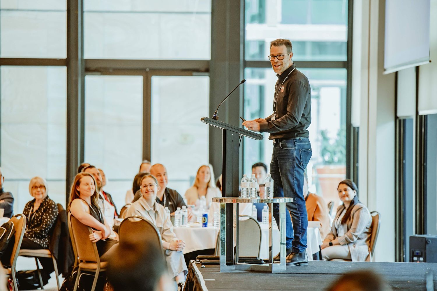 Speaker presenting to audience members at a business conference in modern glass venue.