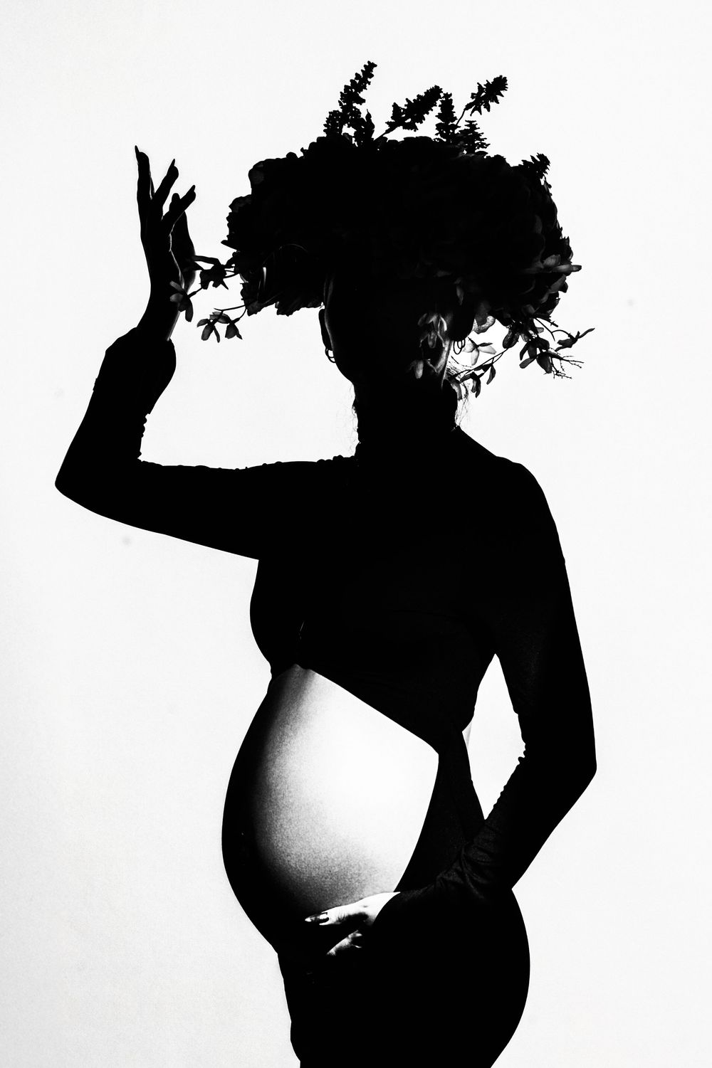 Black and white silhouette of pregnant woman wearing floral crown on white background.