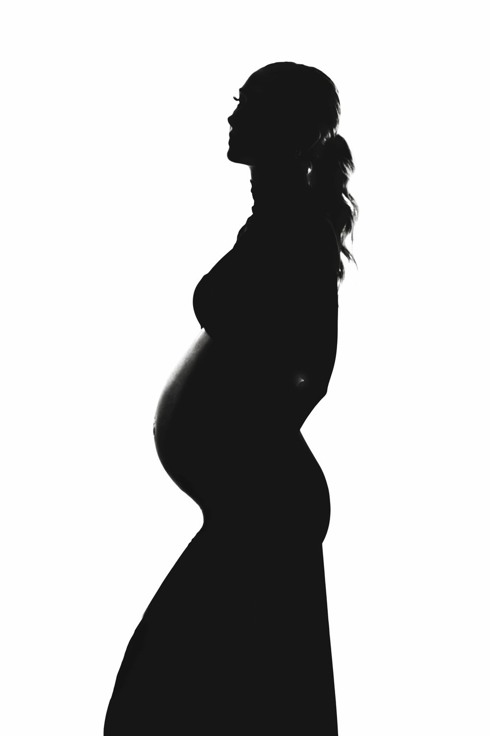 Elegant black and white silhouette of a pregnant woman in profile against white background.