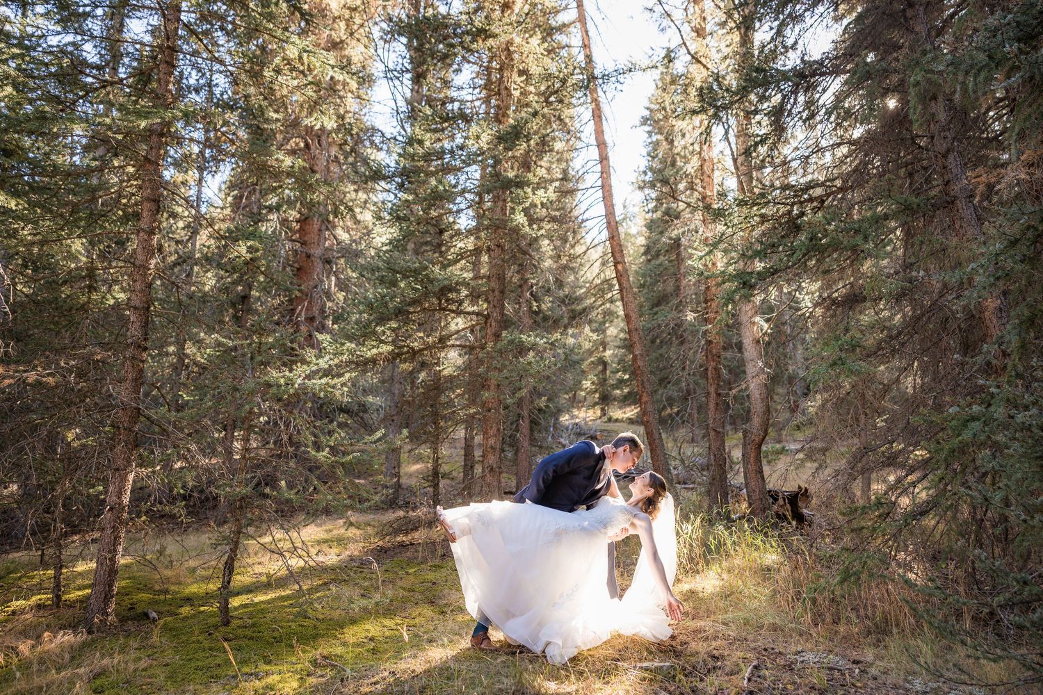 A couple walks hand in hand through a scenic wooded mountain path during a romantic outdoor photoshoot.