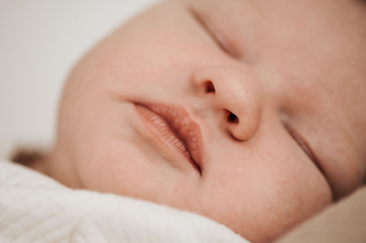 Close-up portrait of a sleeping baby's face with soft, peaceful features against a light background.