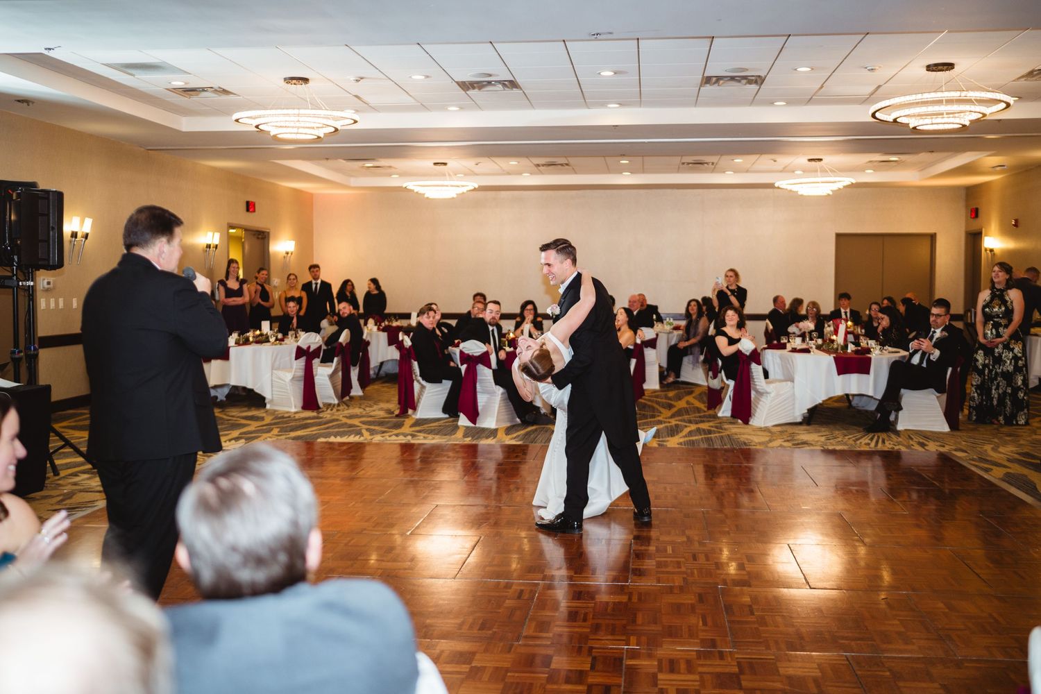 Couples dancing together in an elegant ballroom with warm lighting and polished wooden floors during a formal event.