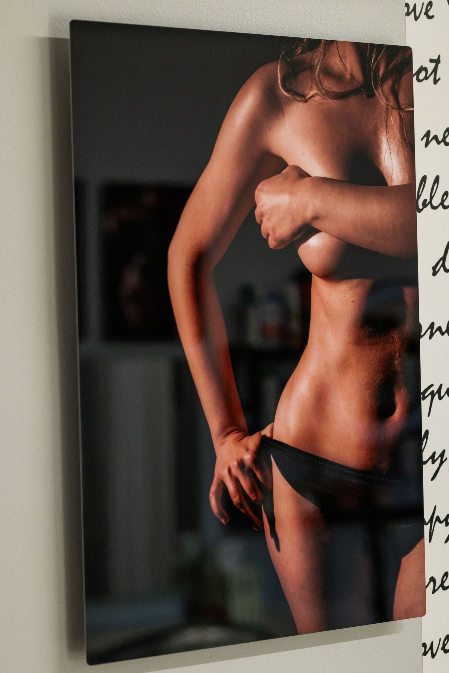 Artistic black and white nude photograph displayed as wall art showing partial torso in dramatic lighting.