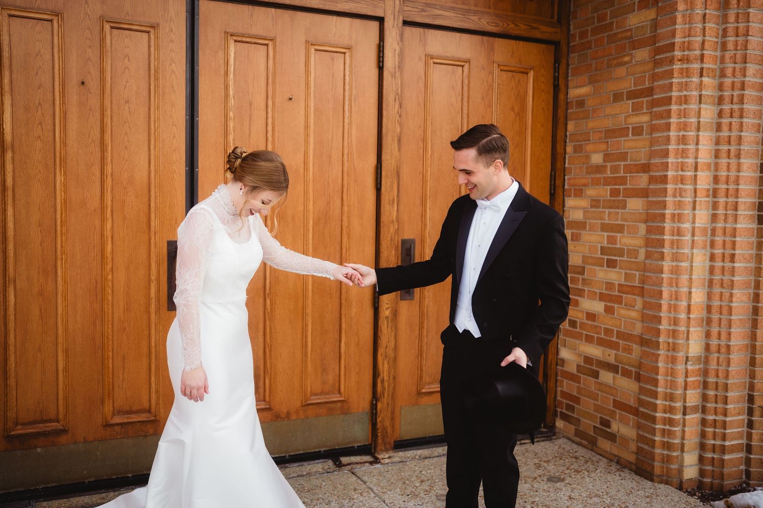 A bride and groom share their first look moment outside wooden doors at a brick church building.