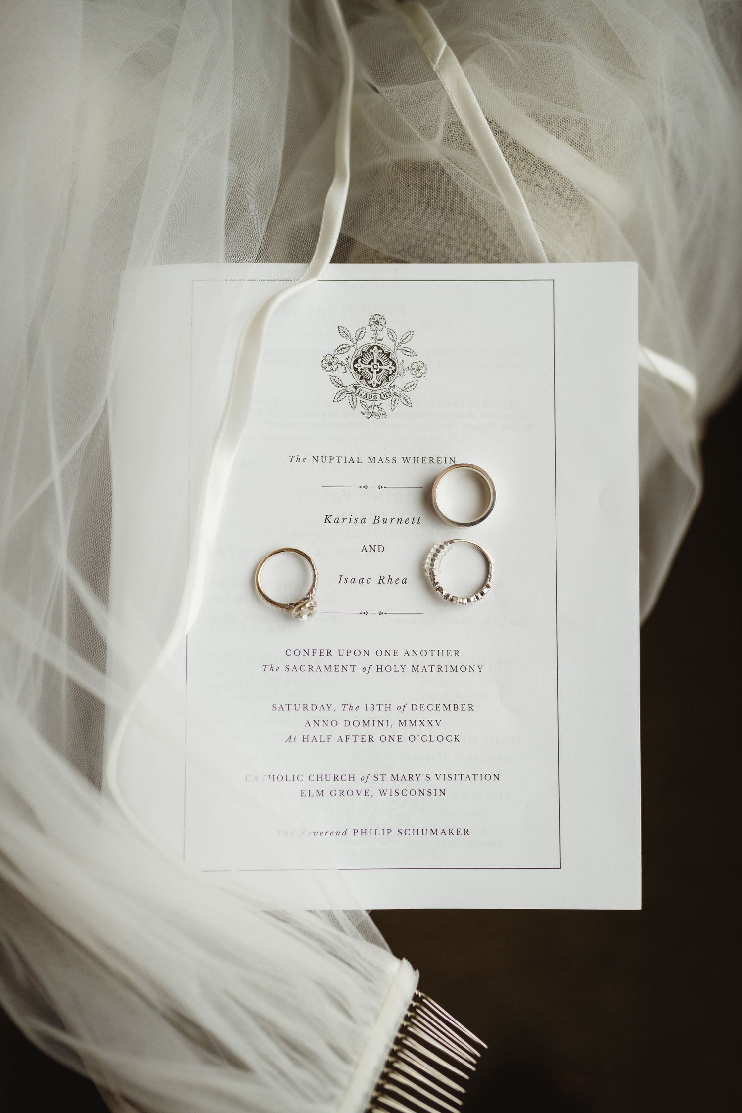 Wedding rings and elegant invitation cards arranged on white tulle fabric with delicate lighting.