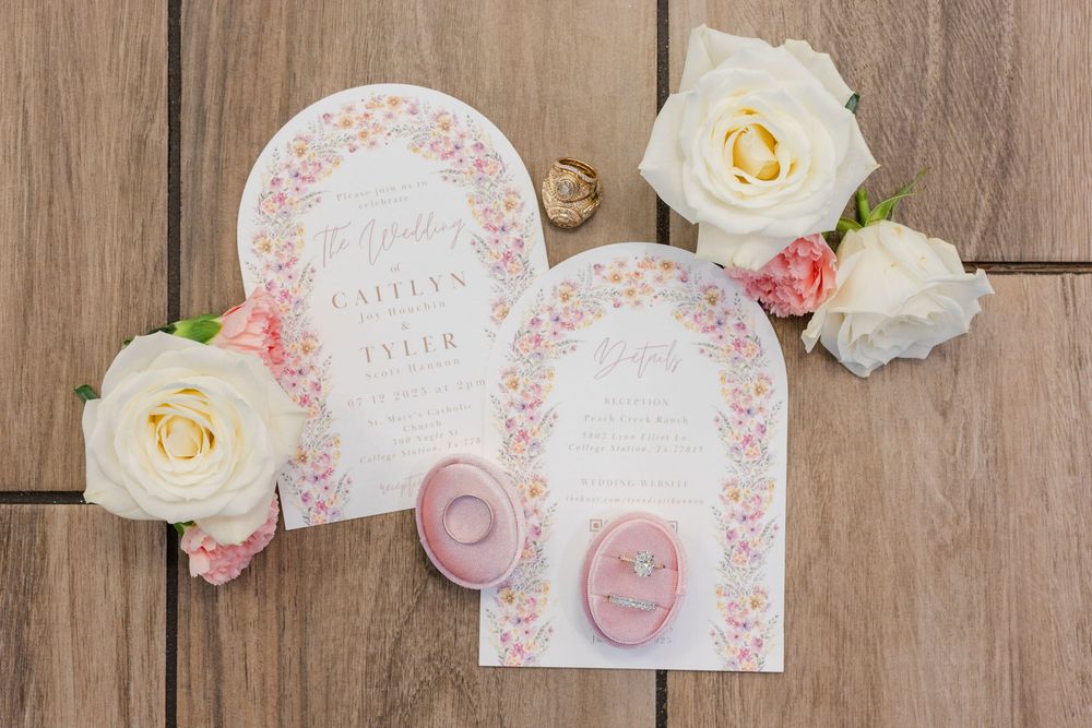 Wedding invitation suite with delicate pink floral designs and white roses arranged on wooden background.