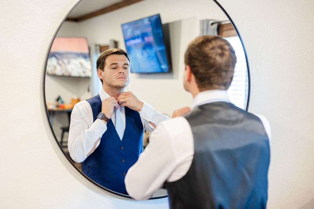 A young man adjusts his tie while looking in a mirror during formal preparation.