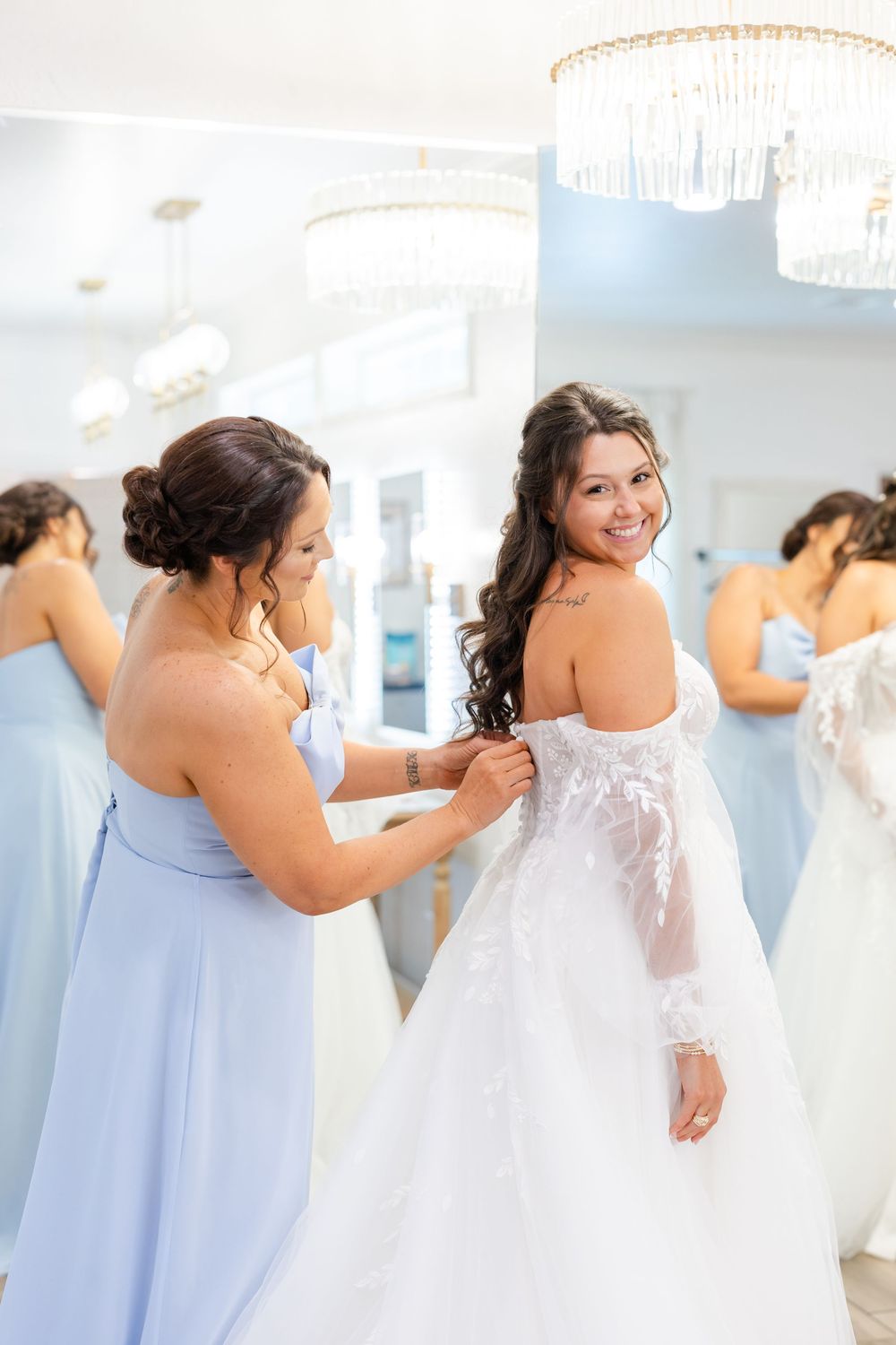 A wedding dress fitting moment in a bright boutique with crystal chandeliers overhead.