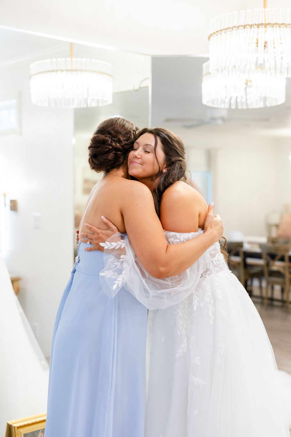 Two women in formal dresses sharing an emotional embrace.