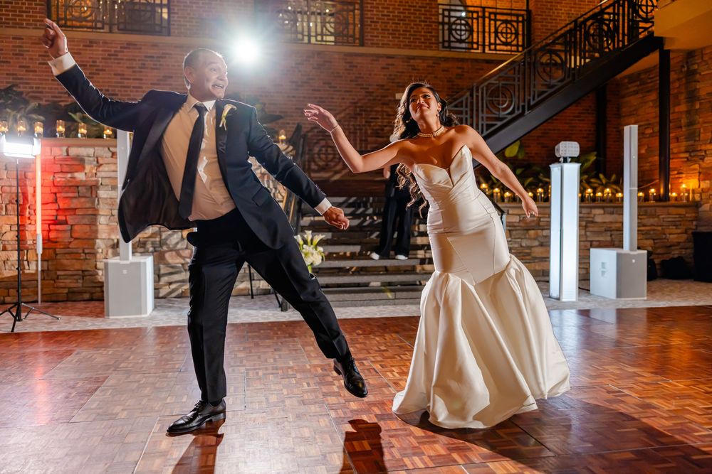 A couple performs an elegant dance move during their first dance at a wedding reception in a rustic brick venue.
