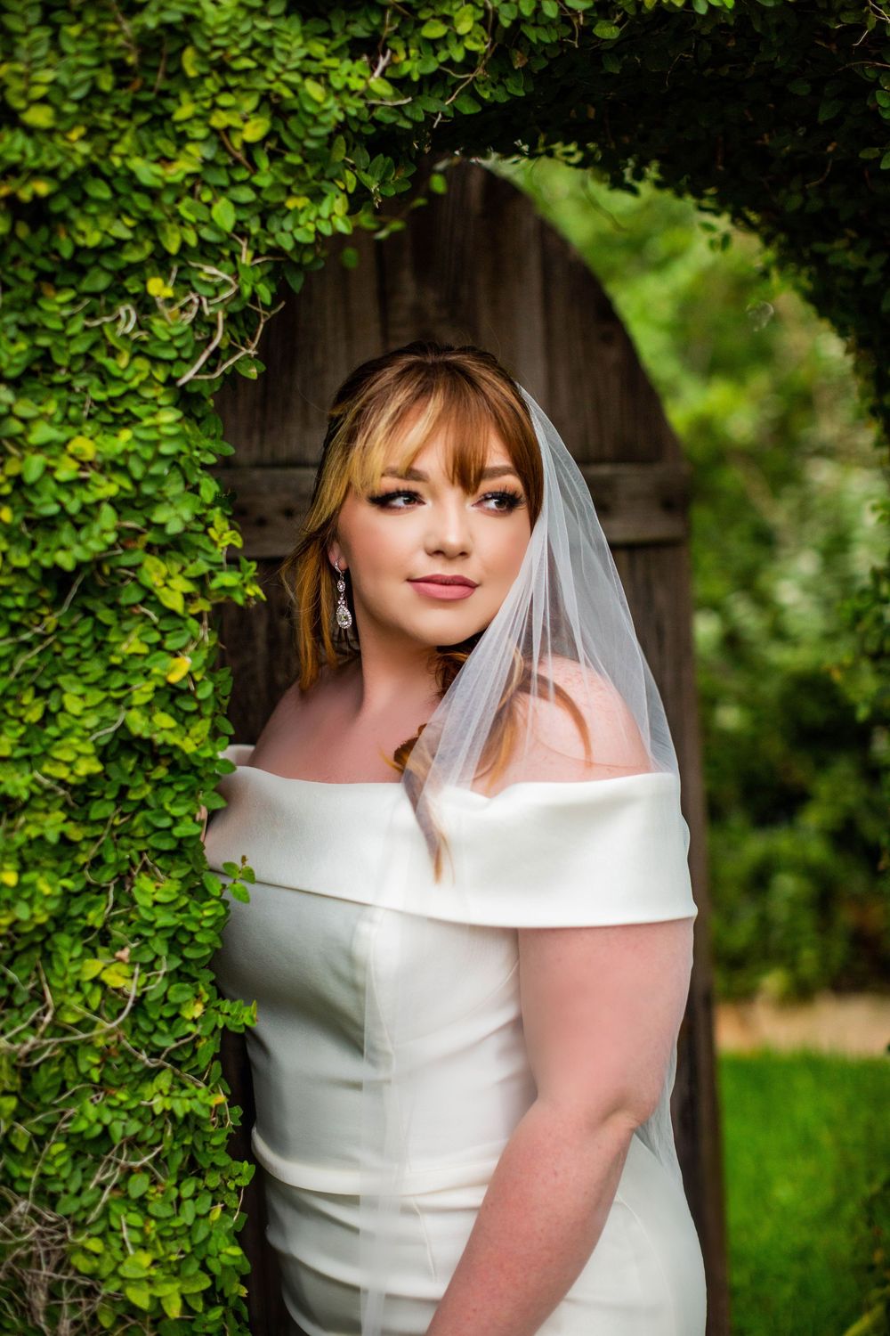 Elegant bridal portrait against lush green foliage and wooden backdrop.