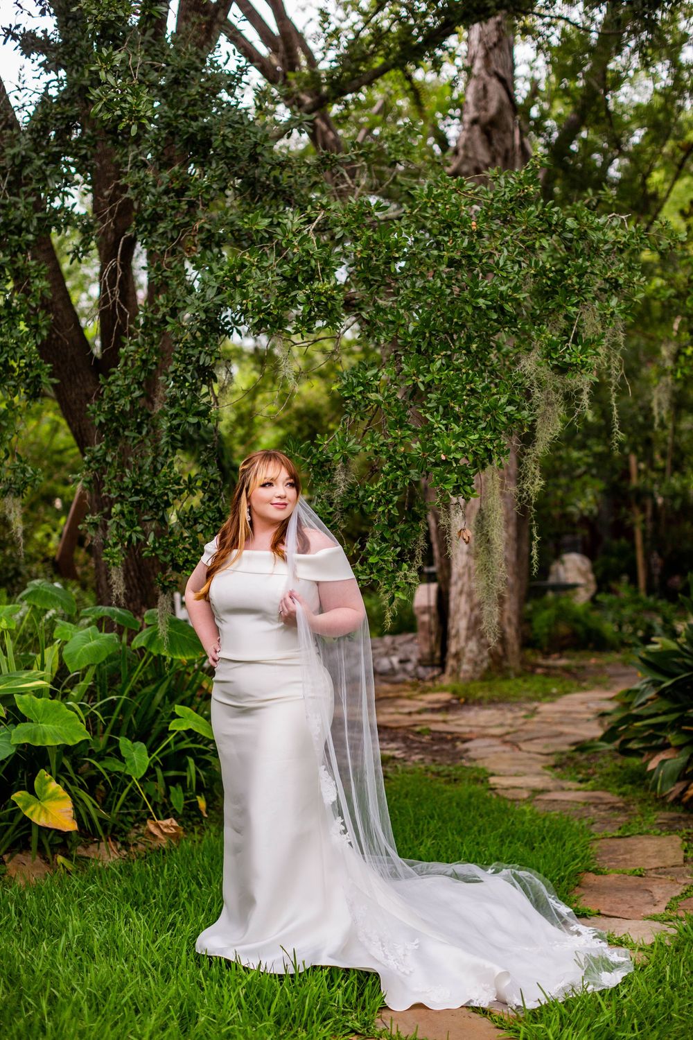 Elegant bridal portrait on garden path surrounded by lush greenery.