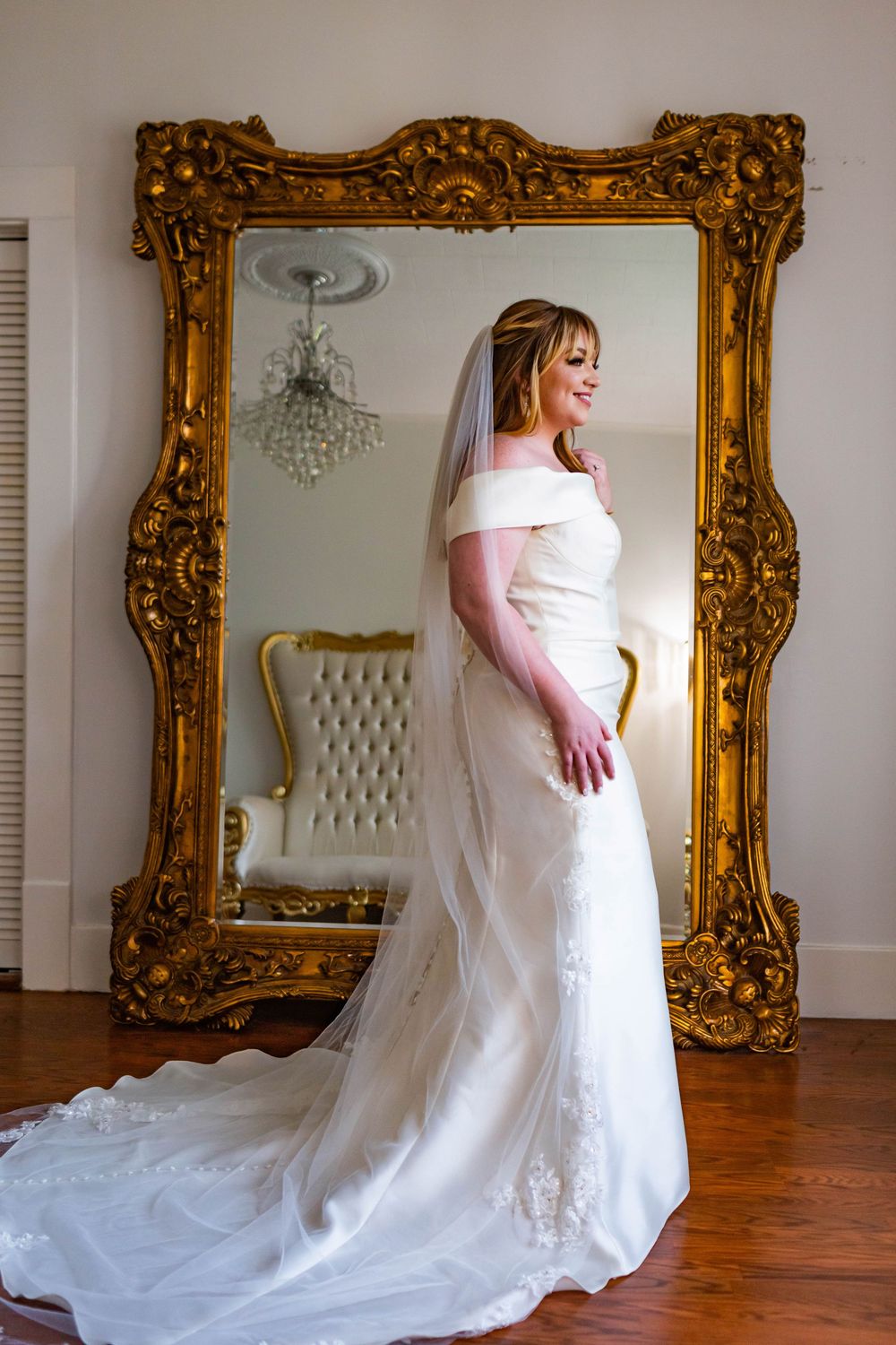 Wedding dress photographed against ornate gold-framed mirrors on white walls.