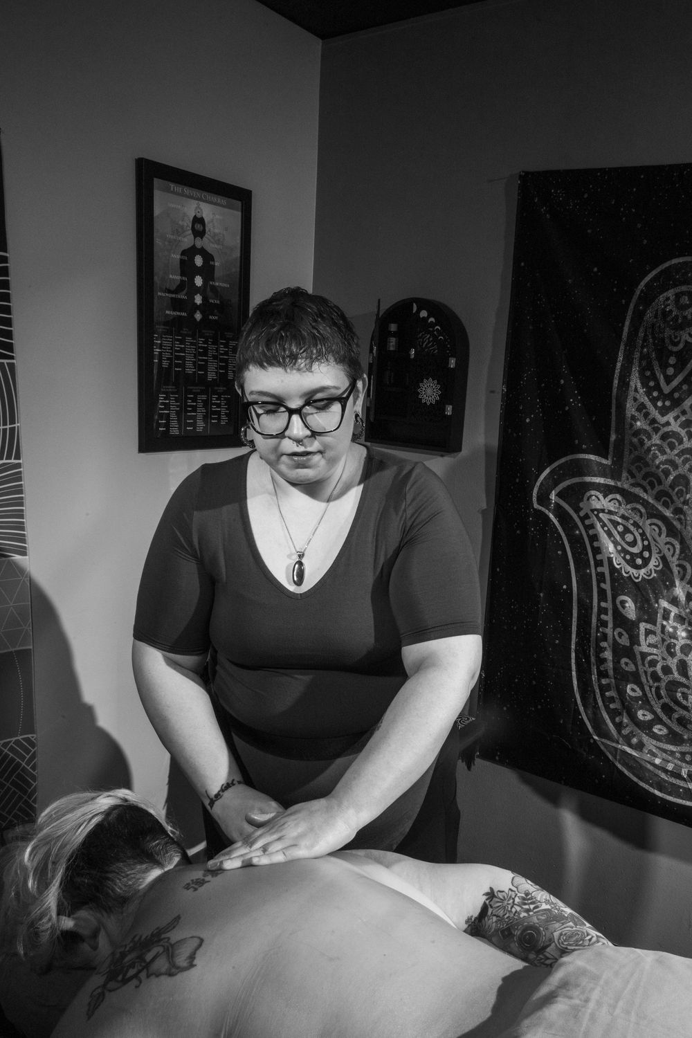 Black and white photo of a massage therapist performing a back massage in a decorated therapy room.